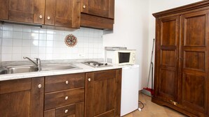A kitchen with wooden cabinets, a white tiled backsplash, a microwave, and a broom. - RESIDENZA LA SCOGLIERA - MONO N° 6 LA SCOGLIERA (Rio Marina)