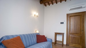 A room with a striped sofa, a wooden door, and an air conditioning unit on the wall.