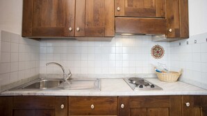 A kitchen with wooden cabinets, a stainless steel sink, a stove, and a tiled backsplash. - RESIDENZA LA SCOGLIERA - MONO N° 8 LA SCOGLIERA (Rio Marina)