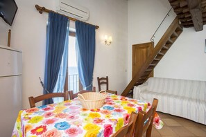 A cozy room with a dining table, a sofa, a wooden staircase, and a window with blue curtains. - RESIDENZA LA SCOGLIERA - LA SCOGLIERA 11 (Rio Marina)