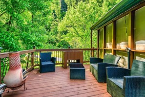 Un terrazzo in legno con mobili in vimini, un vaso grande e vista su fitta vegetazione.