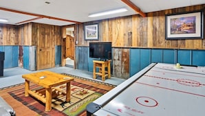 Ein Zimmer mit Holzwänden, einem Fernseher, einem Holztisch und einem Eisstockschiebetisch.