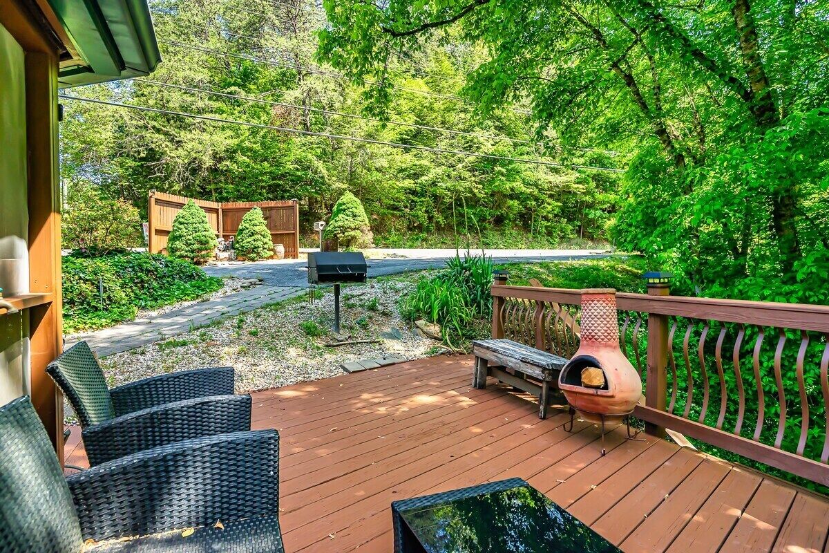 Eine Holzterrasse mit Gartenmöbeln, einem Grill und Blick auf ein bewaldetes Gebiet.