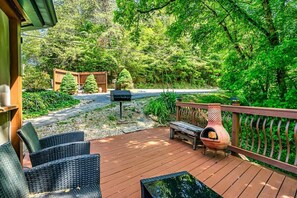 A wooden deck with outdoor furniture, a barbecue grill, and a view of a forested area.