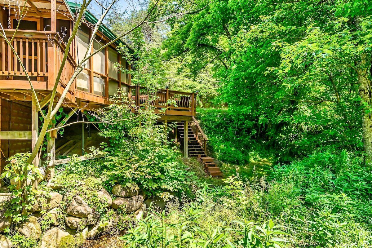 Une cabane en bois avec un escalier menant à une terrasse entourée d’une végétation luxuriante.