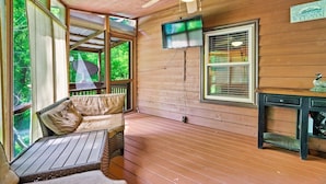 Eine Holzterrasse mit Deckenventilator, einem an der Wand montierten Fernseher und einer mit Kissen ausgestatteten Bank.