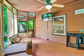 A wooden deck with a ceiling fan, a television mounted on the wall, and a bench with cushions.