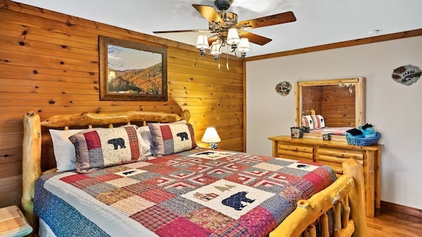 Ein Schlafzimmer mit Holzboden, einem Bett, einem Deckenventilator, einem Nachttisch, einer Kommode und einem Spiegel.