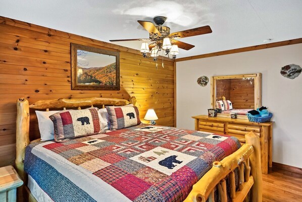 A wooden bedroom with a bed, a ceiling fan, a nightstand, a dresser, and a mirror.