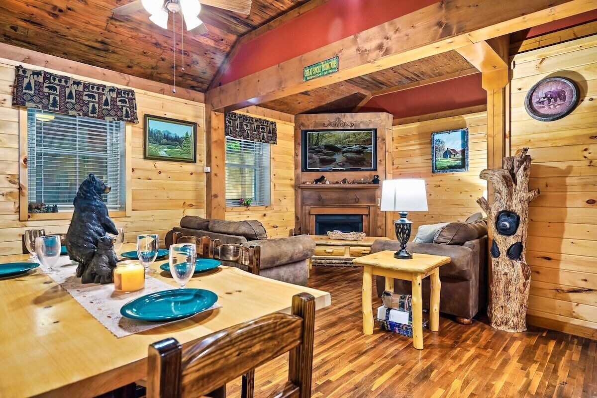 A cozy cabin interior with a dining area, sofas, a fireplace, and wooden walls.