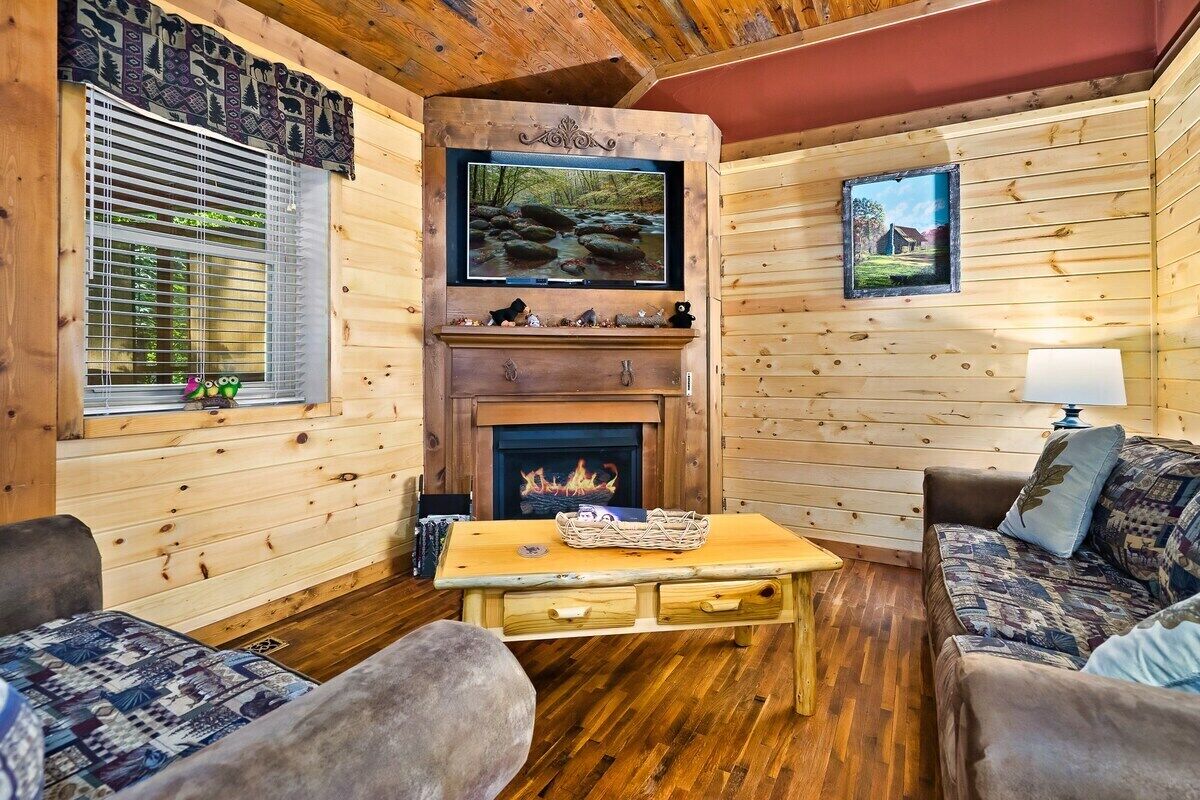 A cozy cabin interior with a fireplace, wooden walls, a television, and a sofa.