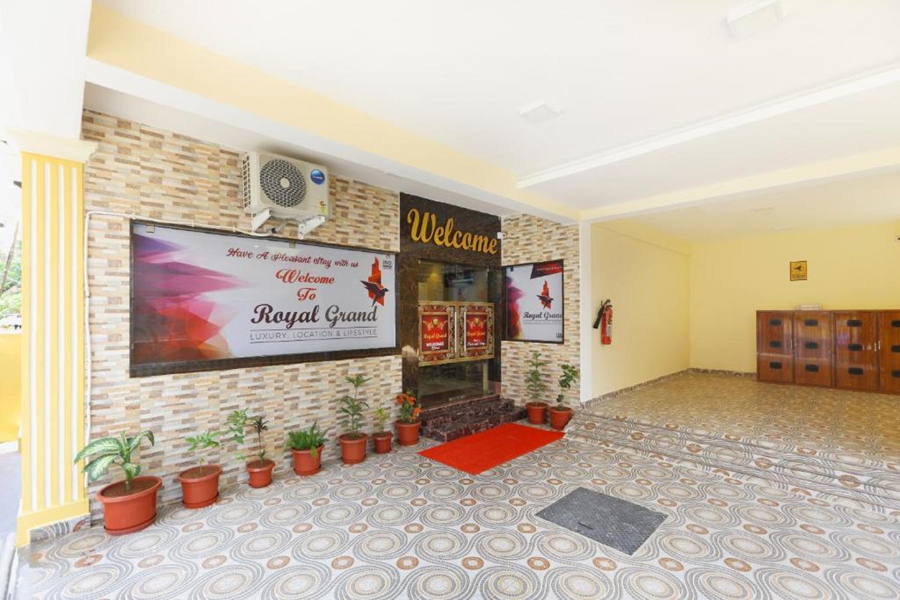 A lobby with a 'Welcome' sign, a 'Royal Grand' banner, and a patterned floor.