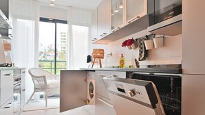 Una cocina moderna con lavadora y secadora integradas, armarios blancos y un amplio ventanal con vistas a la ciudad.