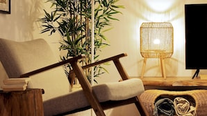 Un salón moderno con una silla de madera, una lámpara de pie trenzada y una planta grande en maceta.