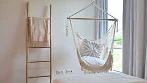 Una habitación con cama, una silla hamaca, una escalera y vistas al exterior.