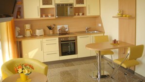 Una cucina compatta con forno a microonde, forno e lavello, una piccola zona pranzo con tavolo e sedie, e una sedia gialla con un vaso di fiori.
