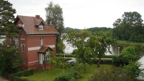 Una casa in mattoni rossi con tetto spiovente, circondata da vegetazione lussureggiante e un lago.