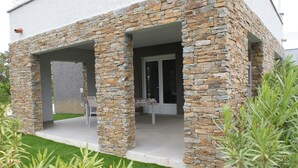 Um edifício moderno com paredes externas de pedra, um espaço de estar coberto e um gramado bem cuidado.