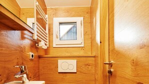 Ein kleines Badezimmer aus Holz mit Waschbecken, Toilette und einem Fenster über der Toilette.