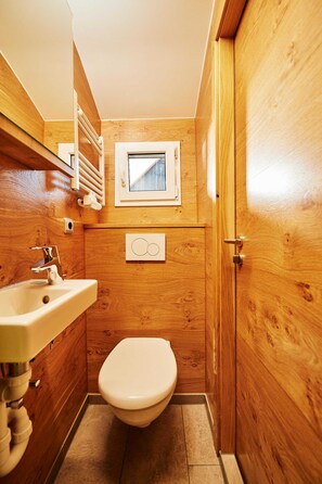 Un bagno in legno compatto con lavandino, water e un piccolo oblò sopra il water.