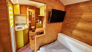 Ein kompakter Raum mit Holzvertäfelung, einem Bett, einer kleinen Küchenzeile und einem an der Wand montierten Fernseher.