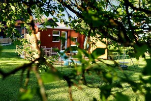 Ein rotes Haus mit einer kleinen Terrasse, einer Schaukel und einem Trampolin im Garten.