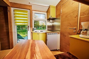 A compact kitchen with a wooden table, a sink, a dishwasher, and a window overlooking a garden. - Schäferwagen Skudde - Handwerkerhof Fränkische Schweiz - Schäferwagen Skudde (Gräfenberg)