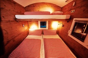 Una baita con due letti, un letto a castello e una finestra con tende.