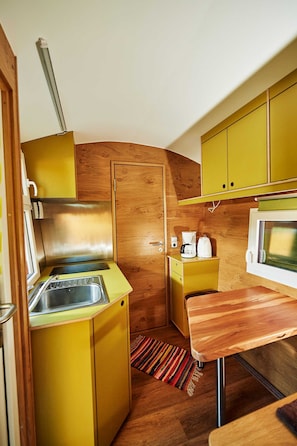 A compact kitchen with yellow cabinets, a stainless steel sink, a microwave, and a wooden countertop. - Schäferwagen Skudde - Handwerkerhof Fränkische Schweiz - Schäferwagen Skudde (Gräfenberg)