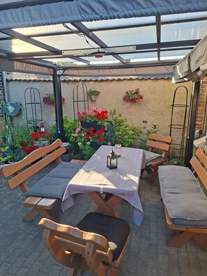 An outdoor patio with a table and benches, surrounded by potted plants and flowers.