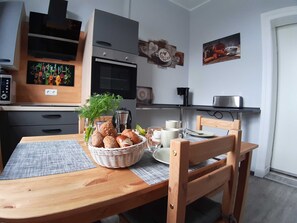 A wooden dining table with a basket of bread, a coffee pot, and a plate.