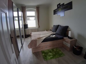 A bedroom with a bed, bedside tables, a lamp, a green rug, and a window with curtains.