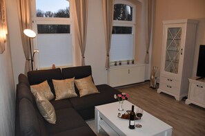 A living room with a dark brown sofa, a white coffee table with a bottle and glass, and a cabinet with glass doors.