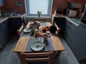A small kitchen with a dining table set for two, a sink, cabinets, and a window with blinds.