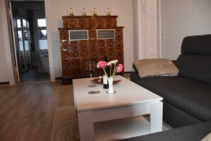 A living room with a dark sofa, a white coffee table with a vase of flowers, and a wooden cabinet with decorative lights.