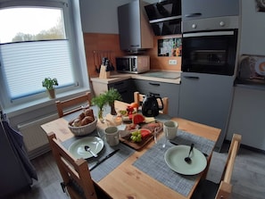 Eine kompakte Küche mit Esstisch für zwei Personen, einer Mikrowelle, einem Backofen und einem kleinen Fenster mit Jalousien.
