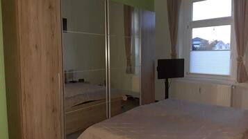 Ein Schlafzimmer mit Bett, Kleiderschrank, Fernseher und einem Fenster mit Vorhängen.