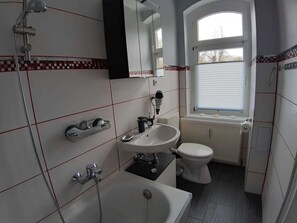 A bathroom with a bathtub, sink, and toilet, a window, and a mirror.