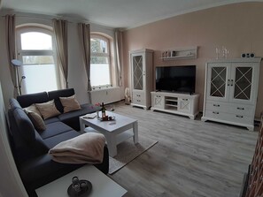 A living room with a sofa, coffee table, TV, cabinets, and a radiator.