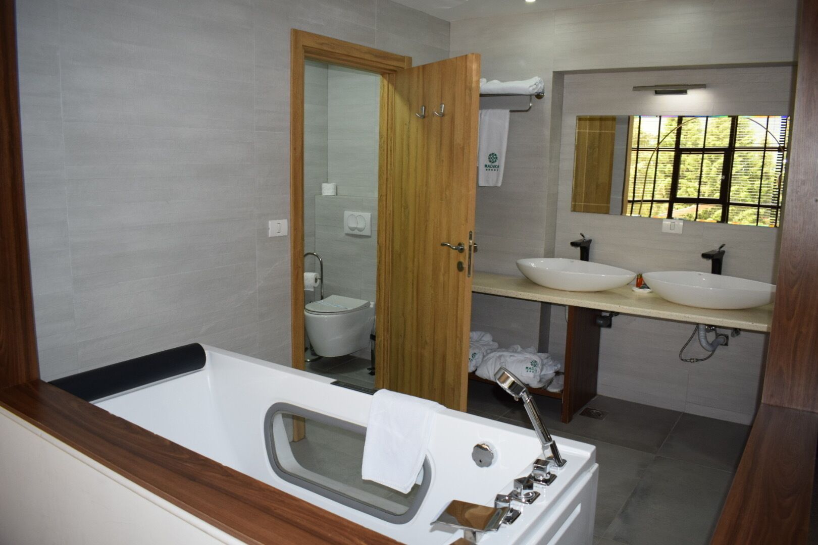 A modern bathroom with a bathtub, two sinks, a toilet, and a large mirror.