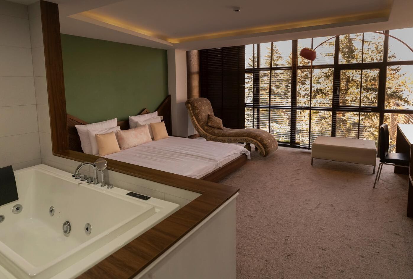 A modern bedroom with a large bed, a sitting area, and a bathtub.