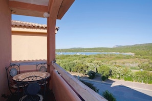 Un balcon avec une table et des chaises, donnant sur un paysage côtier verdoyant avec une étendue d’eau.