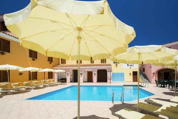 A pool area with yellow umbrellas, lounge chairs, and a building with a tiled roof.