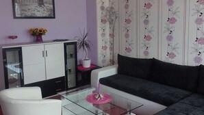 A living room with a glass coffee table, a white sofa, a dark sofa, a cabinet, and a floral wallpaper. - Ferienwohnung Herrmann (Weischlitz)