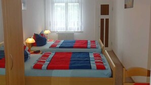 A bedroom with two beds, a window with curtains, a radiator, and a door. - Ferienwohnung Herrmann (Weischlitz)