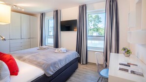 Camera d'albergo con un letto, una scrivania, una sedia, un televisore e una finestra con tende.