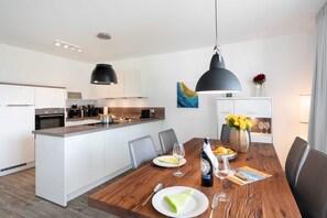 Cozinha moderna com armários brancos, uma ilha de madeira e um espaço de refeições com mesa de madeira, cadeiras e um vaso com flores.