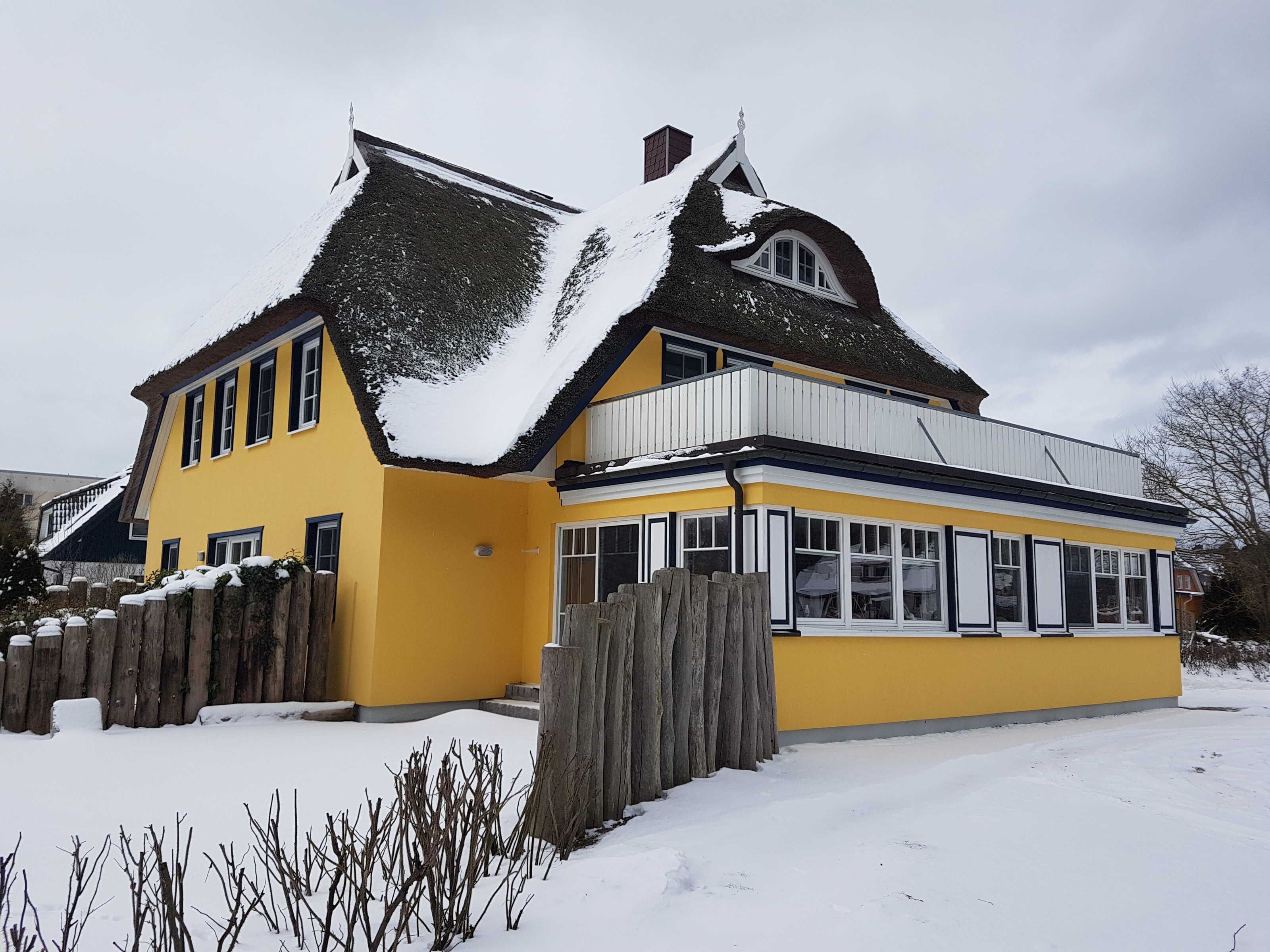 A yellow house with a steep roof and a wooden fence.