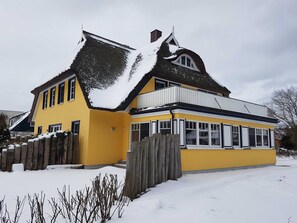 A yellow house with a steep roof and a wooden fence.