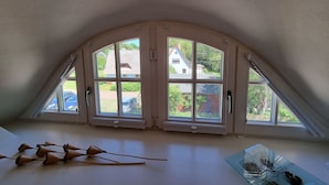 A room with a sloped ceiling, large arched windows, and a glass table. - Buchfink, Deutschland (Prerow)